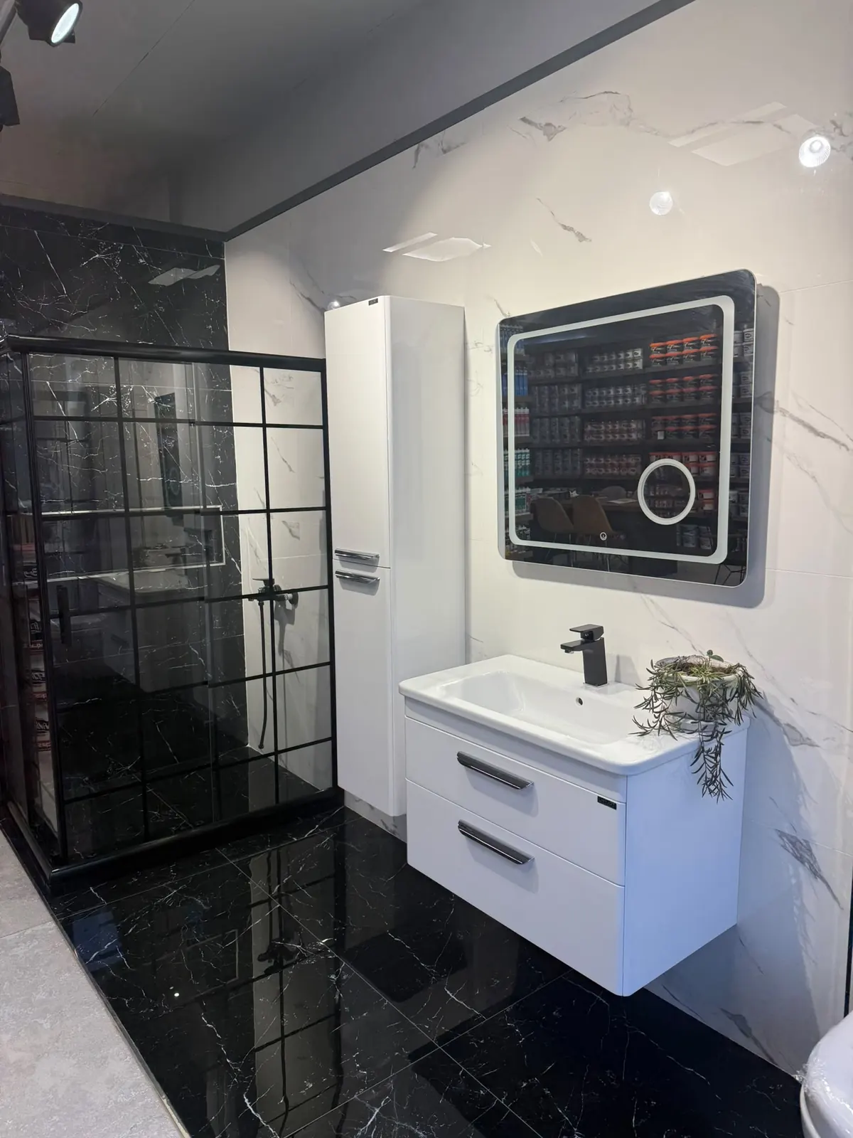 Siyah kafesli duşakabin, beyaz lavabo dolabı ve ışıklı ayna